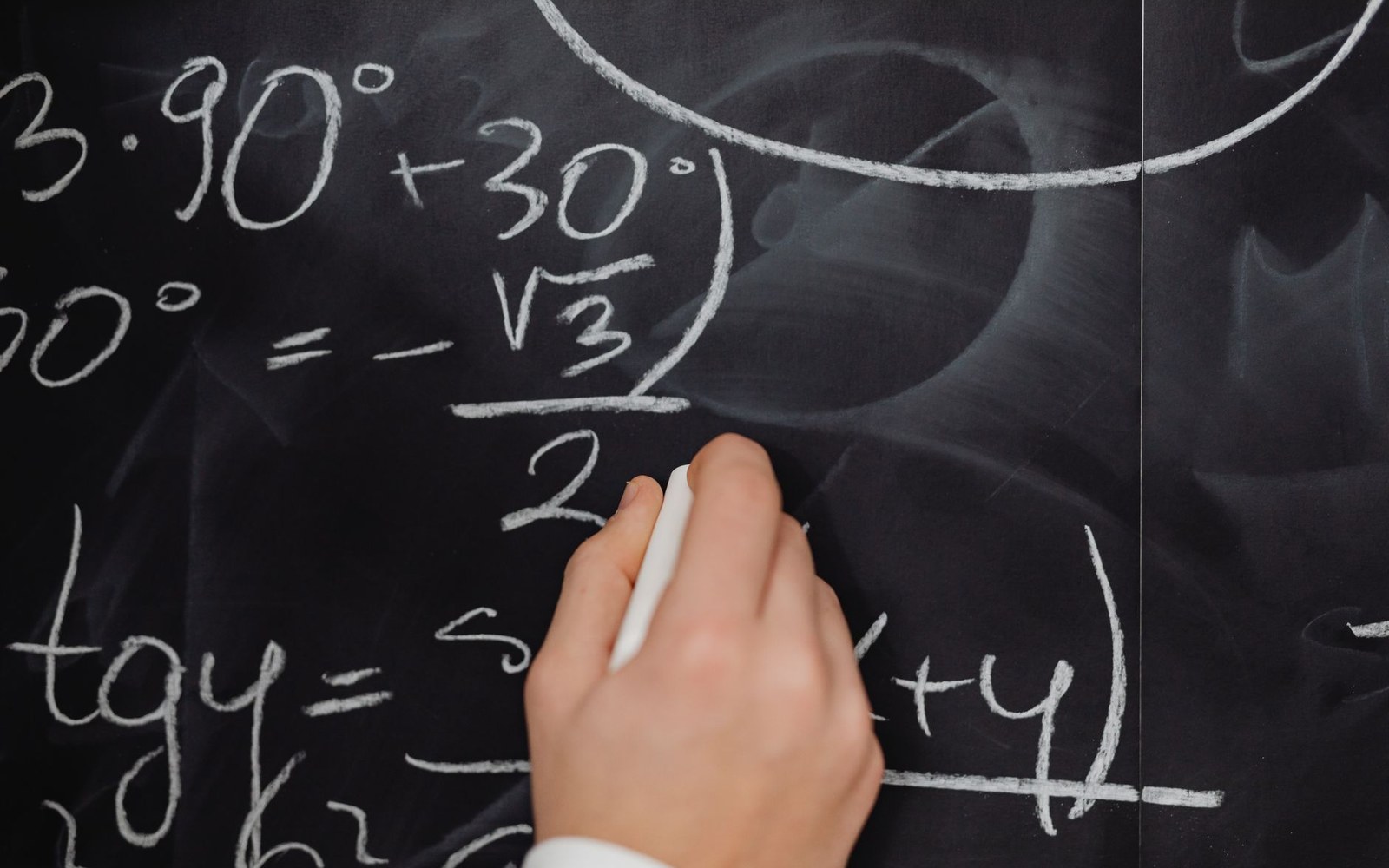 A chalkboard with 10 to the power of minus 60 worked out in full in chalk, adult hand holding the chalk at the right edge of frame