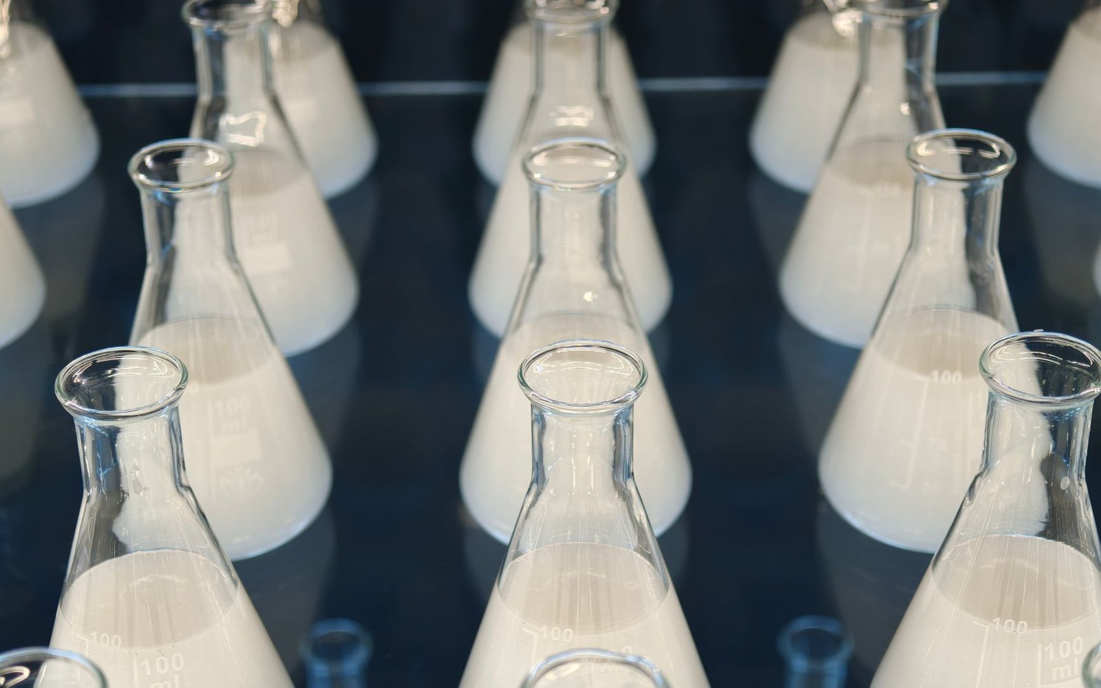 A ranked row of glass dilution flasks on a laboratory bench, an adult researcher's hands adjusting one at the near end