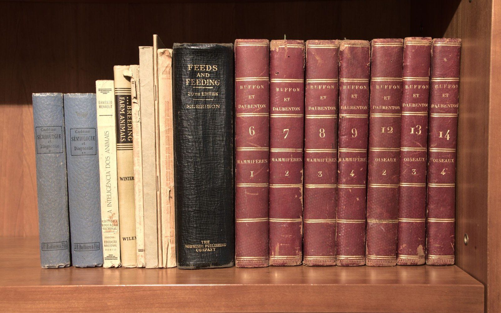 Rows of worn hardcover volumes on farming and animal breeding line a wooden shelf