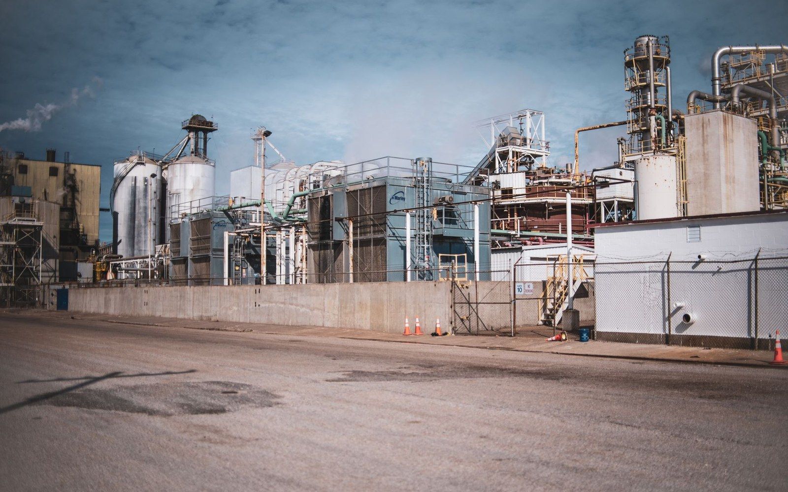 Industrial plant with storage silos, tanks and pipework behind a chain-link fence