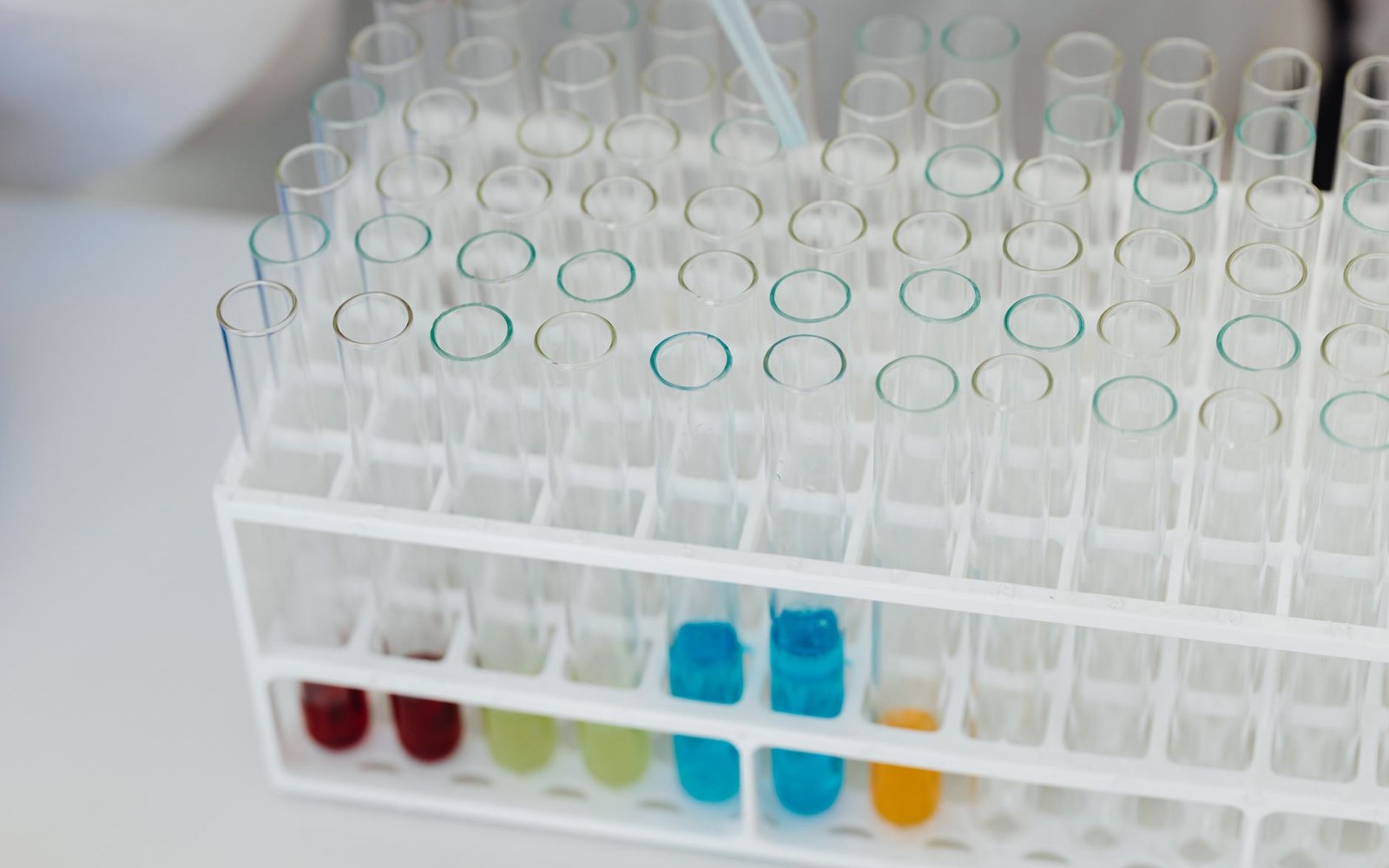 Rows of empty glass test tubes in a white rack with a few holding colored liquids