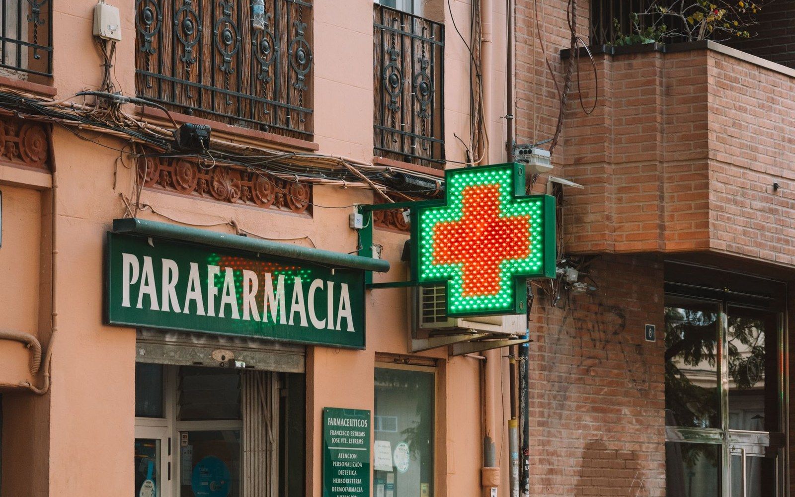 Illuminated green cross sign beside a parafarmacia storefront on a street corner