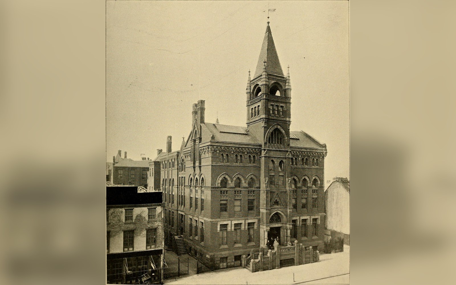 Vintage photograph of a brick building with a tall corner tower and steep spire
