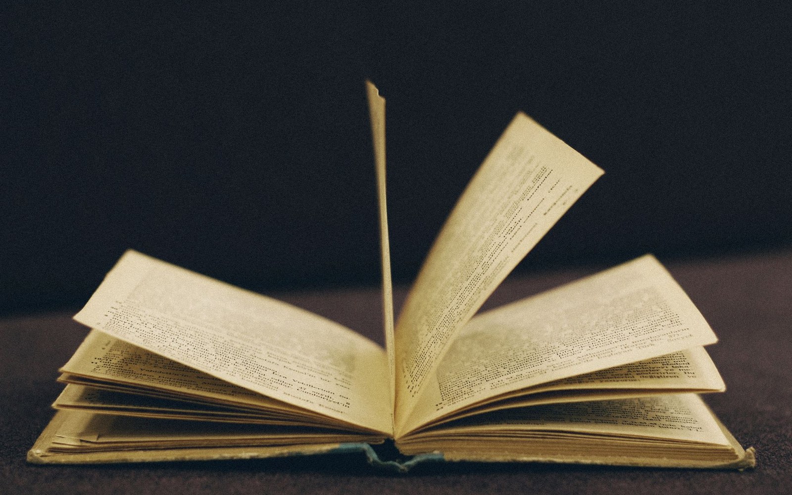An open book with yellowed pages fanned upward against a dark background