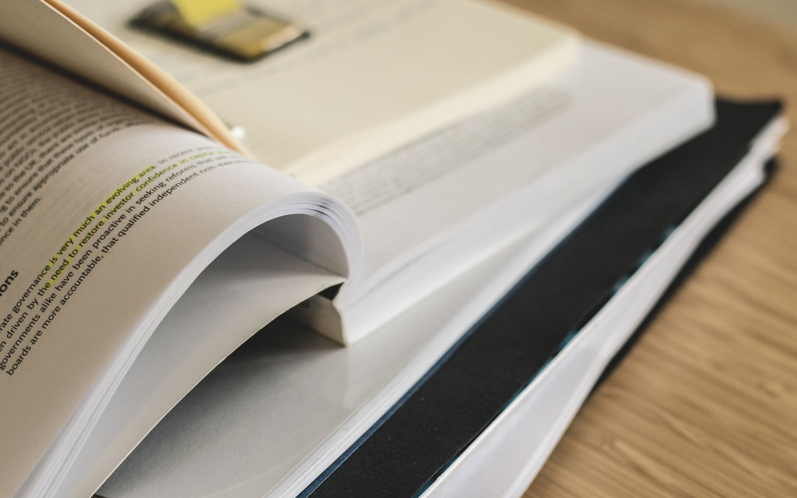 Open book with a sticky note bookmark resting atop a closed hardcover book
