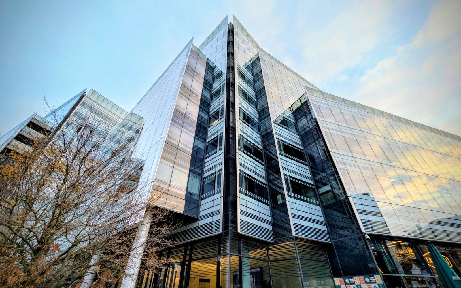 Angular glass office building with a sharply pointed facade against a partly cloudy sky