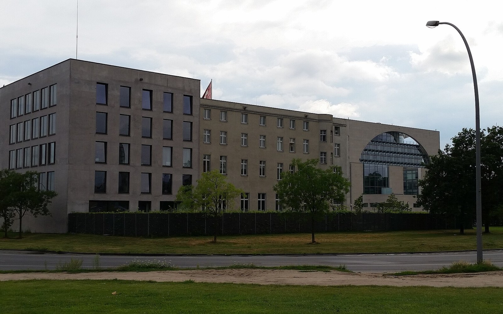 A government building with a hedge-lined perimeter and an arched glass structure visible behind it